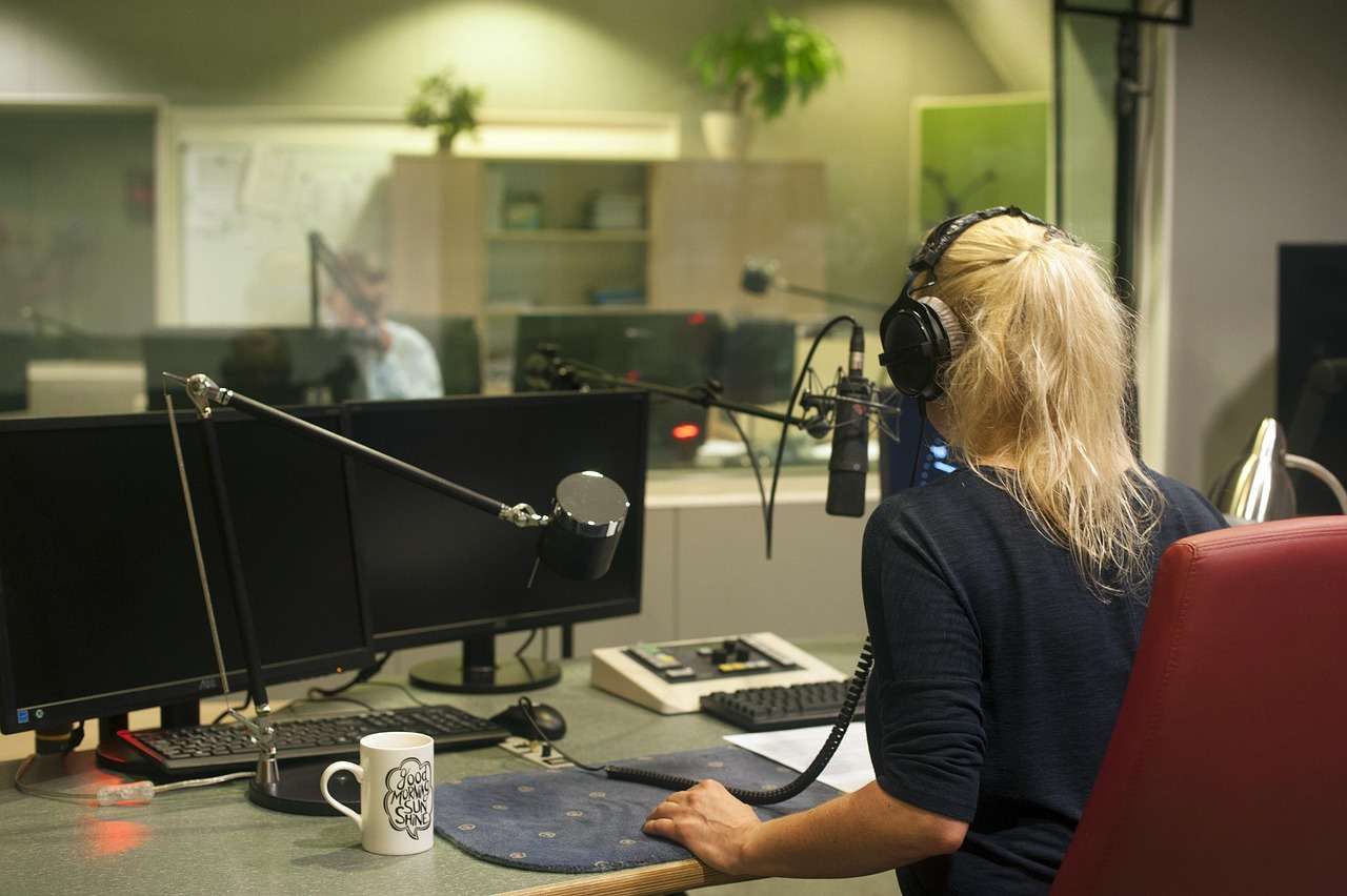 Radio presenter at a broadcast mixing desk with microphone